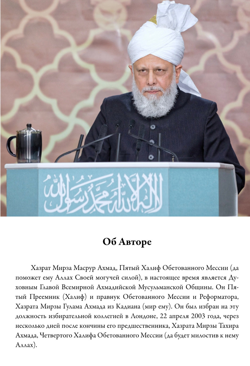 Man in traditional attire speaking at a podium with Arabic text
